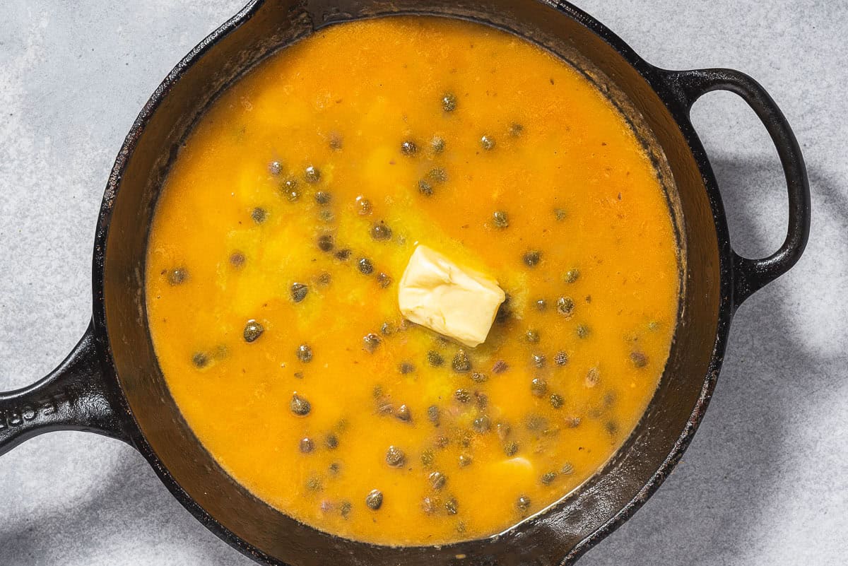 La sauce piccata avec une cuillerée de beurre dans une poêle en fonte.