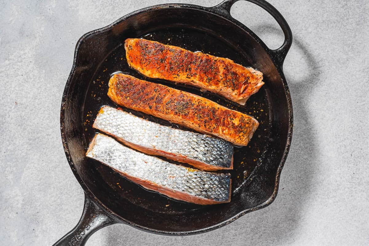 4 filets de saumon saisis dans une poêle en fonte. Deux sont la peau et 2 sont étoffées.