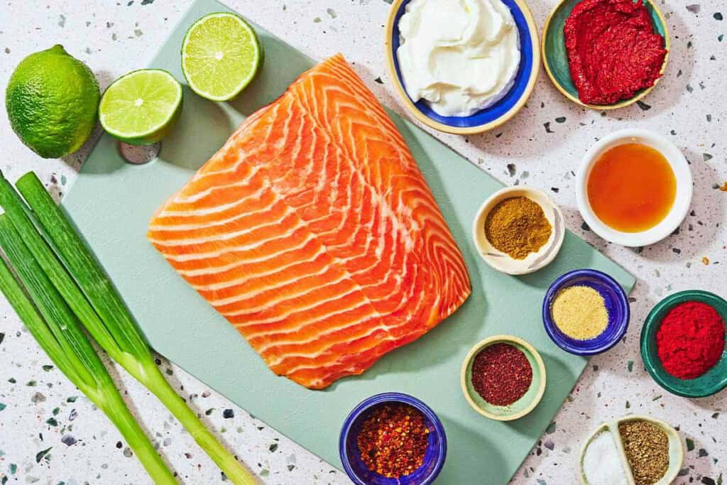 Ingrédients pour les piqûres de saumon, y compris le saumon, les oignons verts, les limes, le yaourt grec, la pâte de harissa, le miel, le paprika espagnol fumé, la poudre à l'ail, les flocons d'Alep, le cumin, le sumac, le sel et le poivre noir.