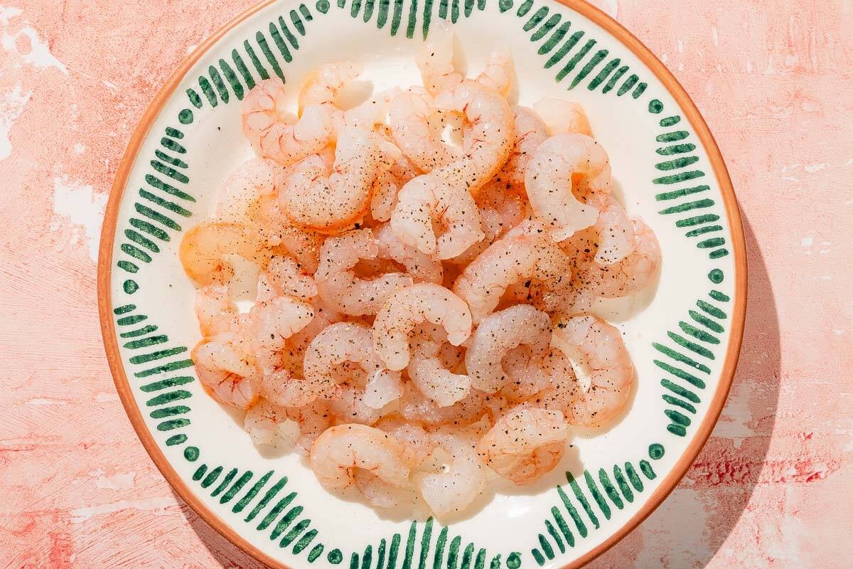 Des crevettes crues assaisonnées de sel et de poivre sur une assiette.