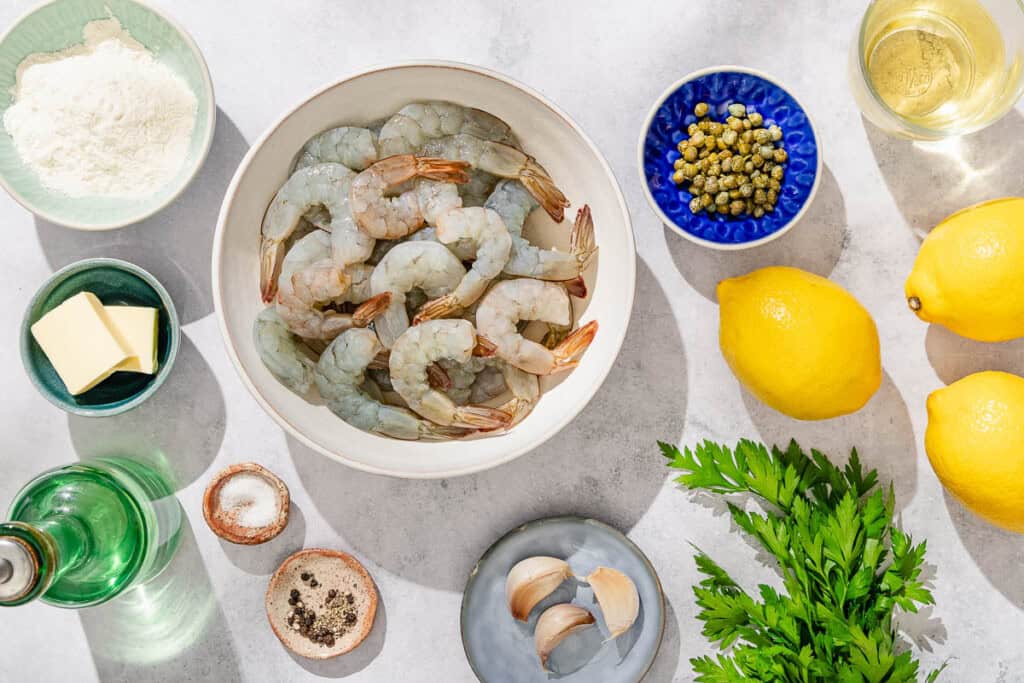 Ingrédients pour les crevettes piccata, y compris les crevettes jumbo, le sel, le poivre noir, la farine, l'huile d'olive, le beurre, l'ail, le vin blanc, les citrons, les câpres et le persil.