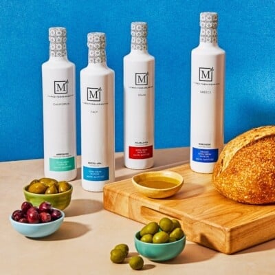 Le paquet d'huile d'olive extra vierge tous les jours de la boîte de vaisselle méditerranéenne deux prochaines 3 bols d'olives et un plateau en bois avec une miche de pain et un bol d'huile d'olive.