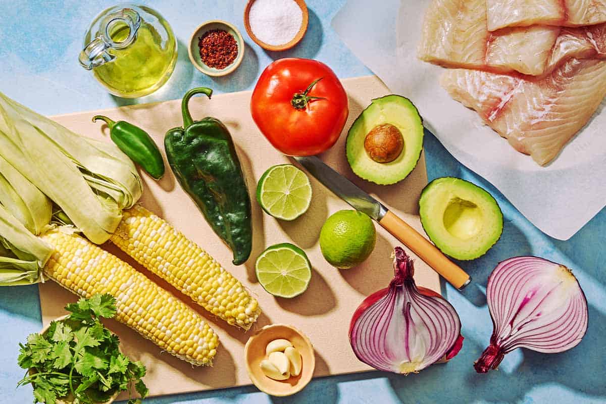 Ingrédients de la plie pochée et de la salsa de maïs sucré, y compris la plie, les oreilles de maïs, la coriandre, l'ail, l'oignon rouge, les limes, un poivre de poblano, un poivre jalapeño, l'avocat, l'huile d'olive, le poivre alep et le sel.