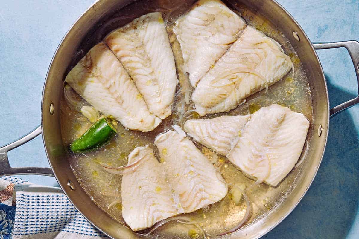4 filets de plie étant pochés dans de l'eau dans une poêle à côte élevé.