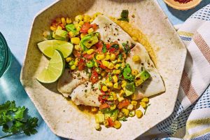 Poached flounder topped with sweet corn salsa on a plate with lime wedges.