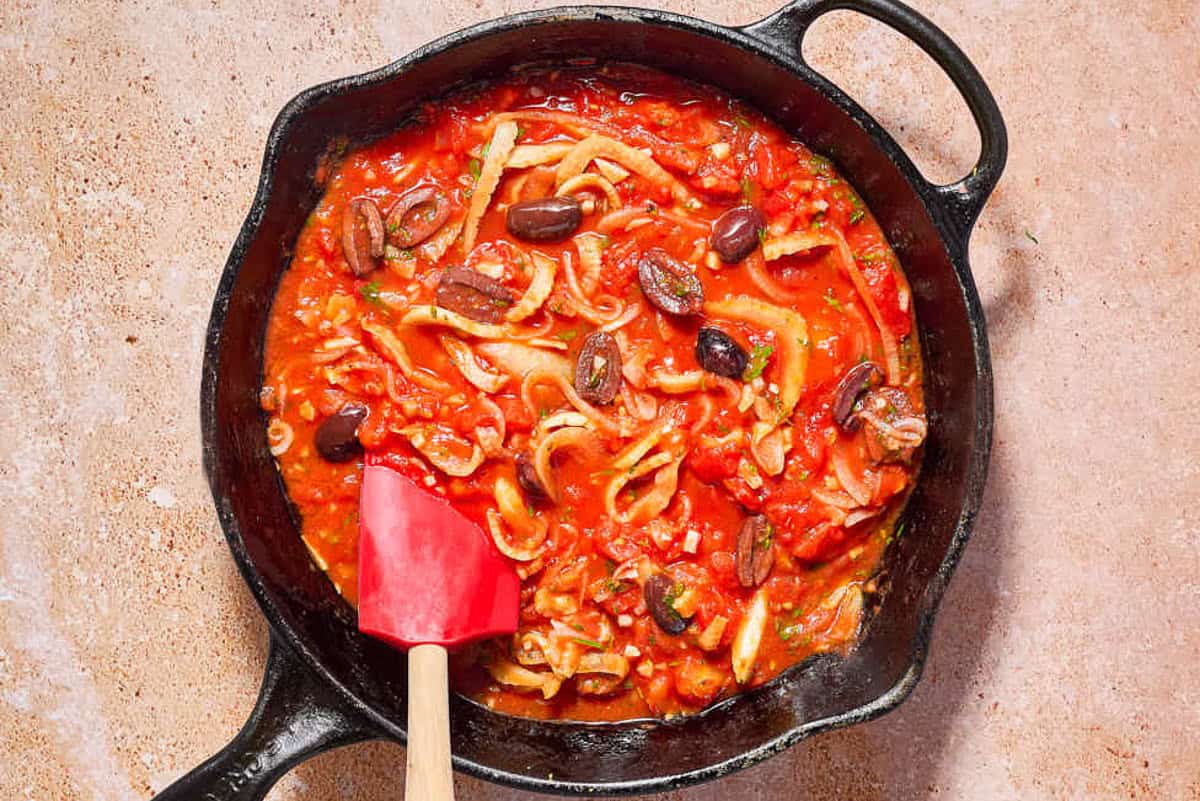 La sauce pour le poisson provençal dans une poêle en fonte avec une spatule.