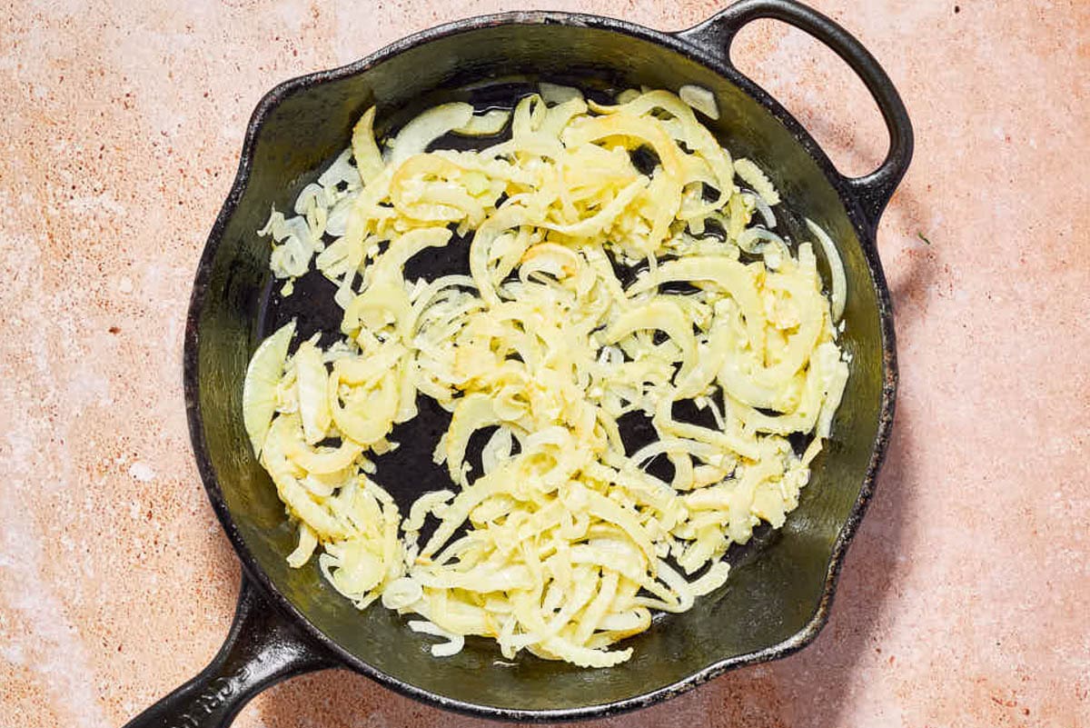 Les oignons tranchés pour le poisson provençal sautent dans une poêle en fonte.
