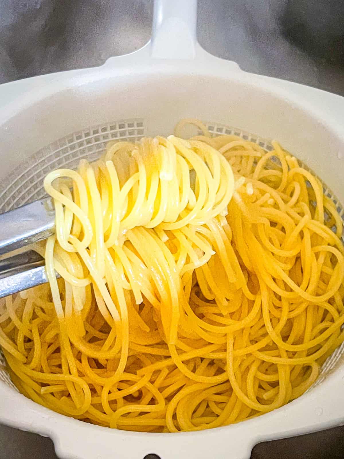 Un bol blanc avec une passoire et des spaghettis.