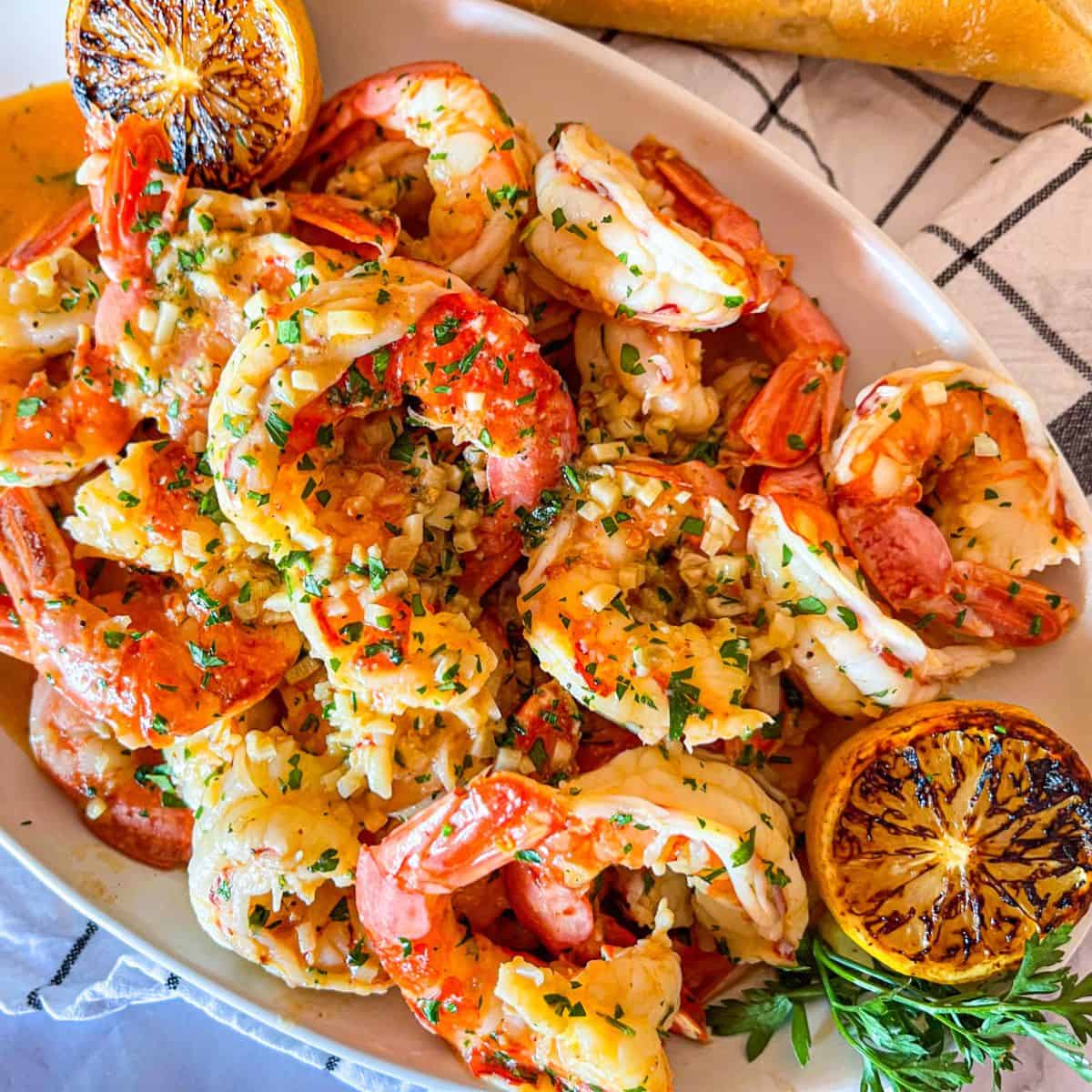 Platter of shrimp scampi without wine garnished with grilled lemon and diced parsley.