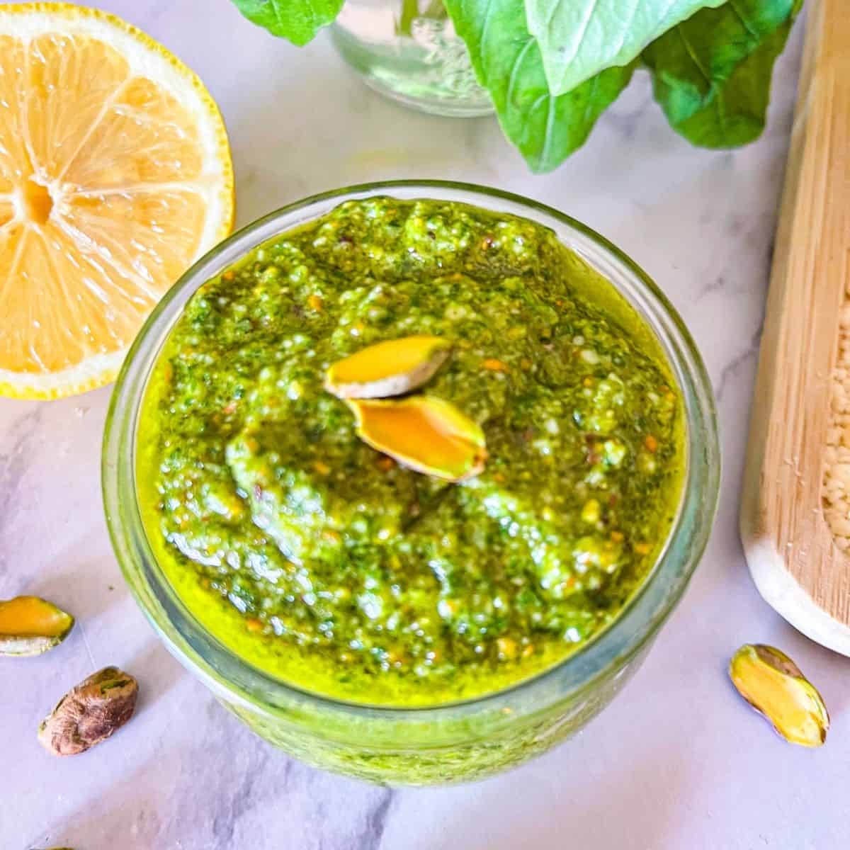 Pistachio Pesto on a table with pistachios around next to basil and lemon.