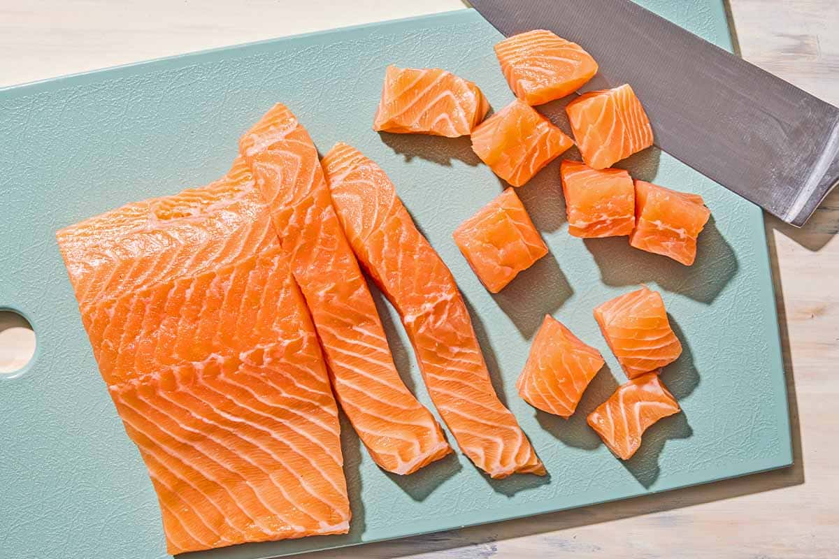 Un filet de saumon non cuit sur une planche à découper avec un couteau. La partie n'est pas coupée, la partie est coupée en bandes et la partie est coupée en cubes.
