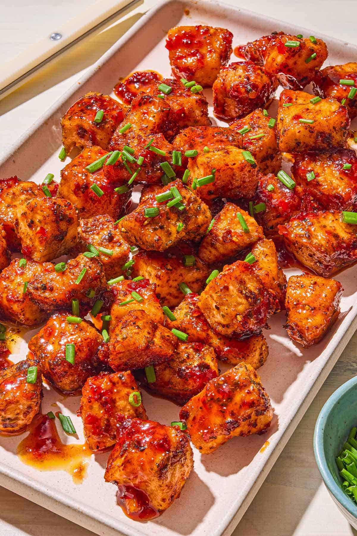 Les bouchées de saumon de friteuse à air garni de ciboulette hachée sur un plateau.