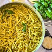 Les pâtes au pesto dans une poêle avec du basilic et du fromage à côté.