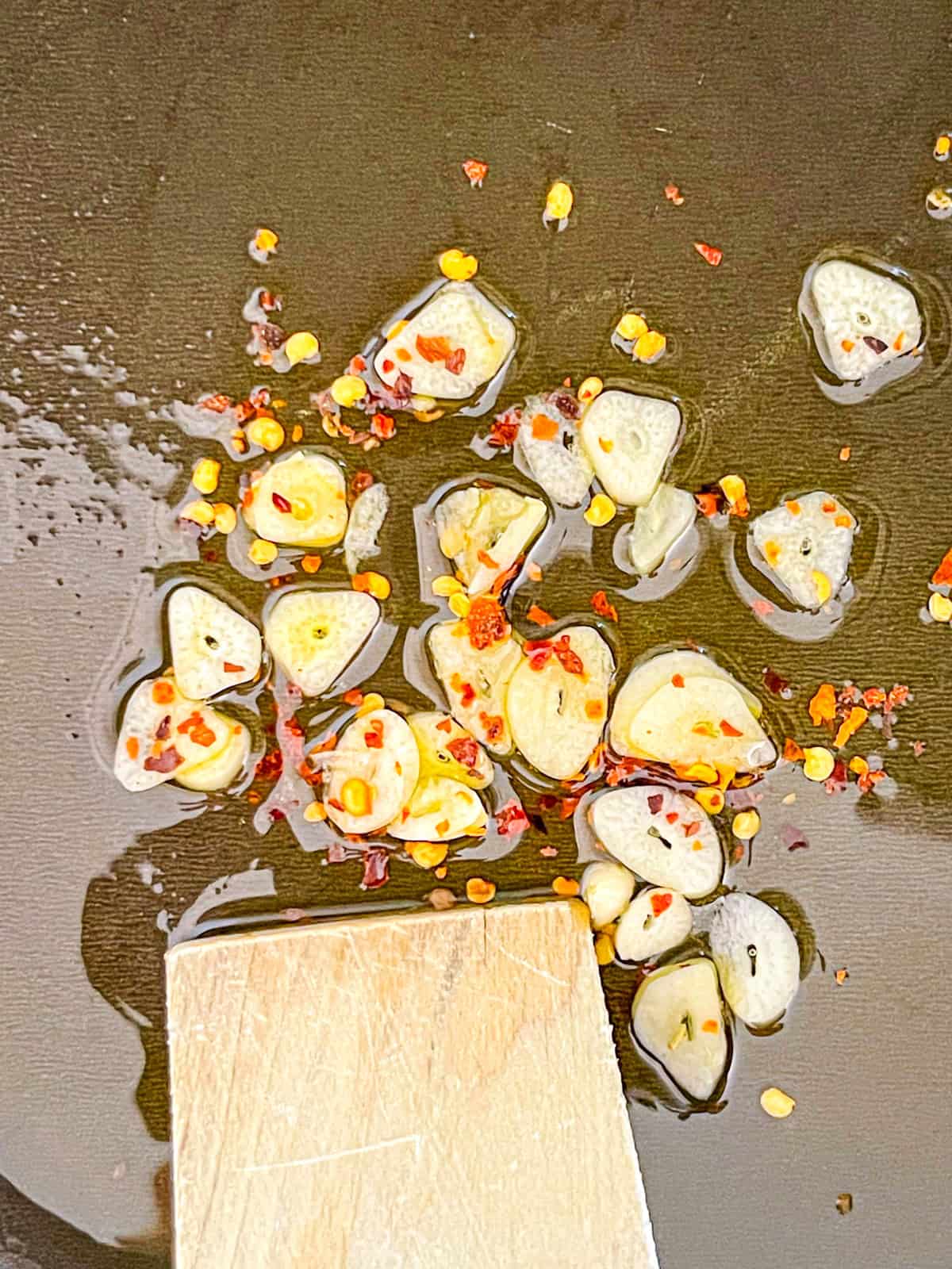 Des flocons d'ail et de poivron rouge sautent dans l'huile.