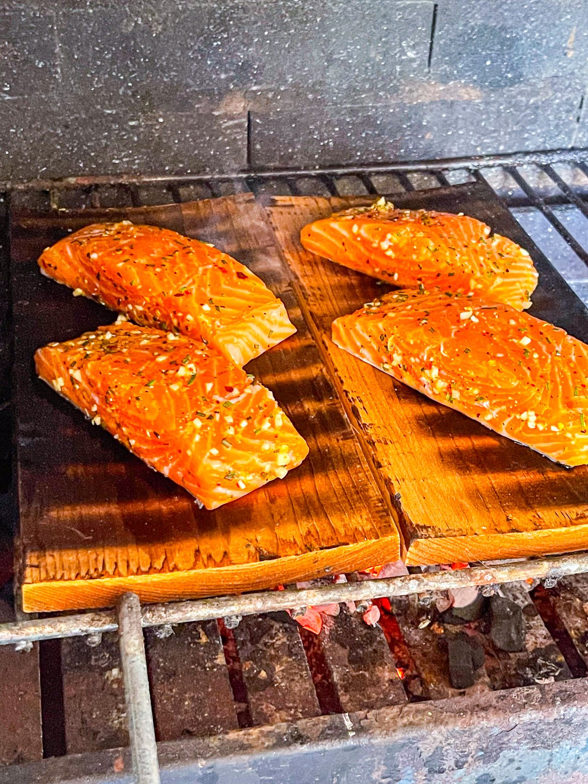 4 filets de saumon cuits sur des planches de cèdre sur un grill au charbon de bois.