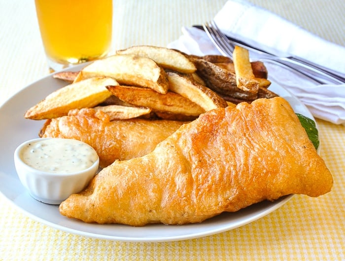 Fish and chips présenté avec une sauce tartare et un verre de bière en arrière-plan