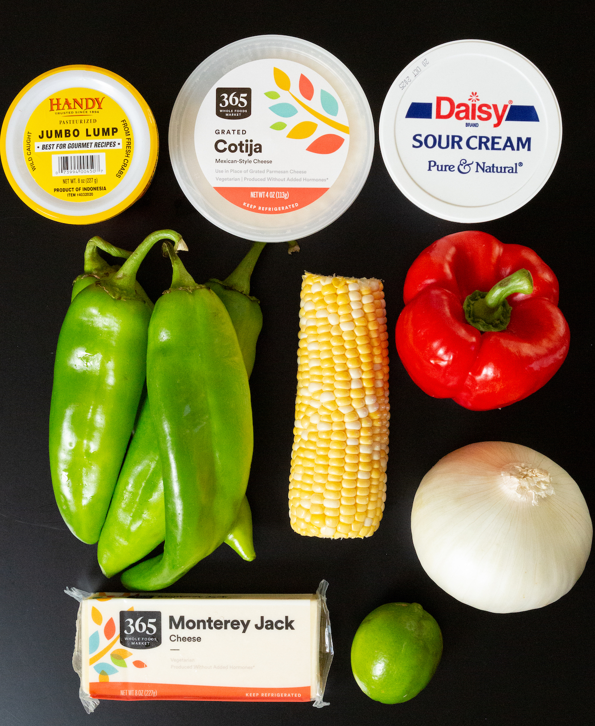 Un contenant de morceaux de crabe, de fromage Donita, de crème sure, de poivrons frais, d'épis de maïs, de poivron rouge, d'un oignon blanc, d'un citron vert et d'un bloc de fromage Monterey Jack.