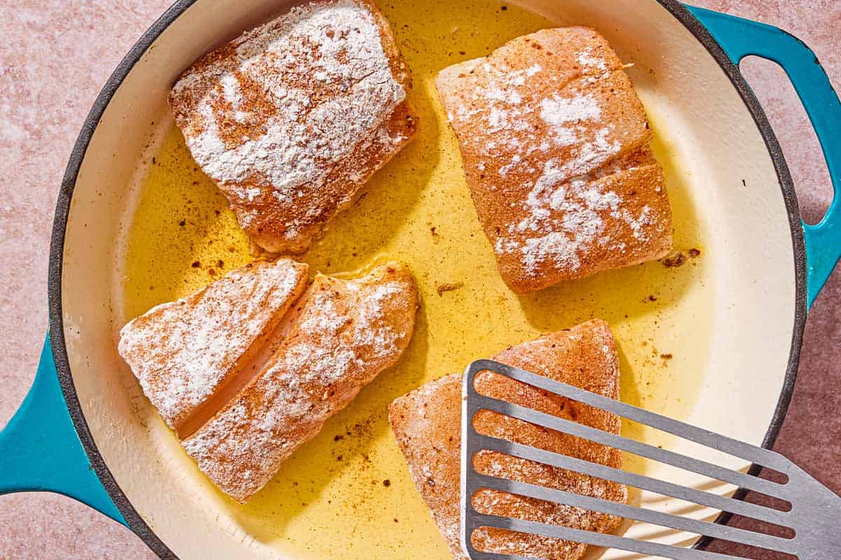Quatre filets de vivaneau frits dans une poêle avec une spatule.