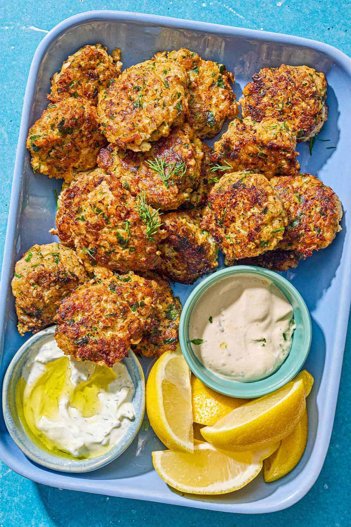 Kofta de crevettes sur un plateau avec des bols de sauce tahini et tzaziki et des quartiers de citron.