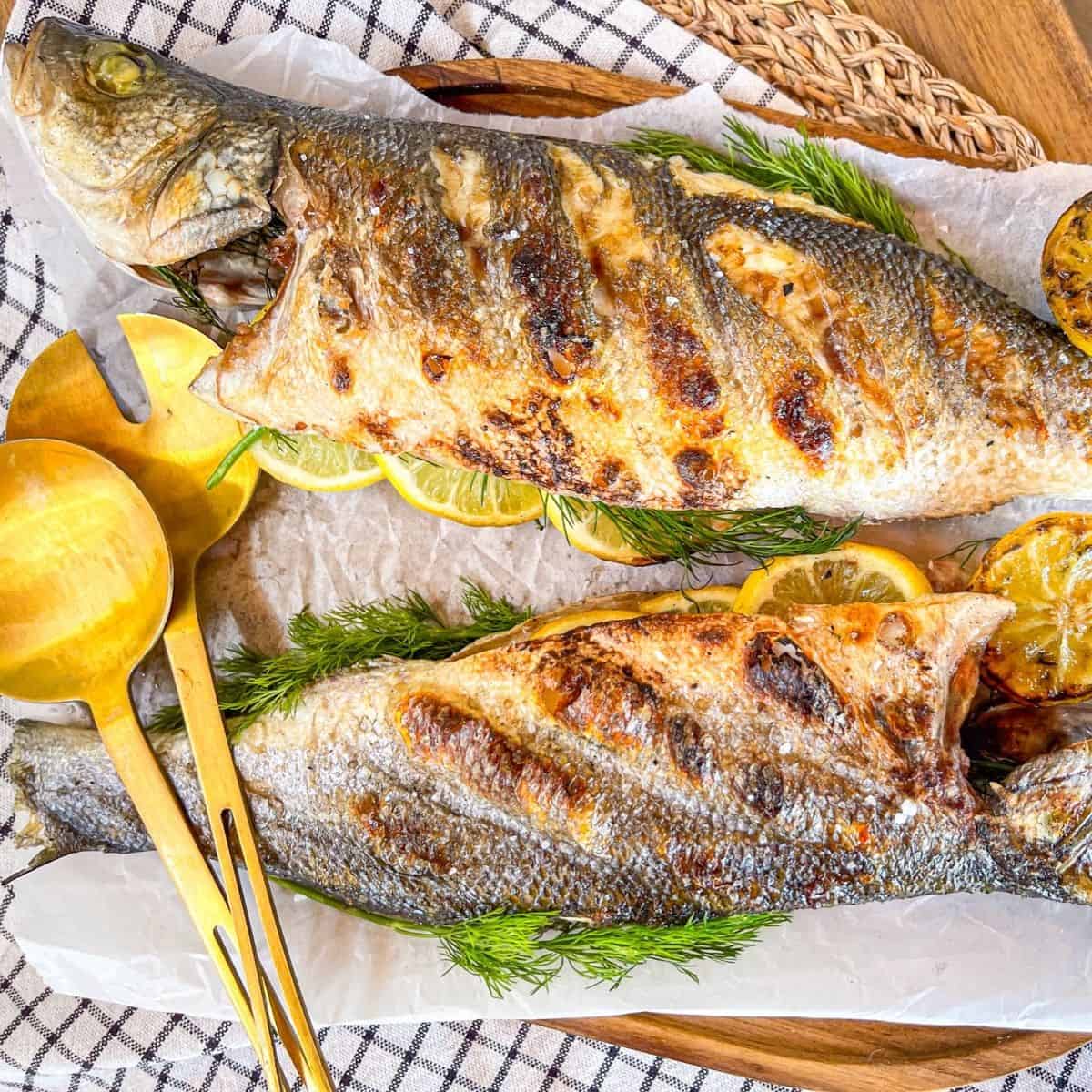 2 whole grilled fish on a platter next to a spoon.