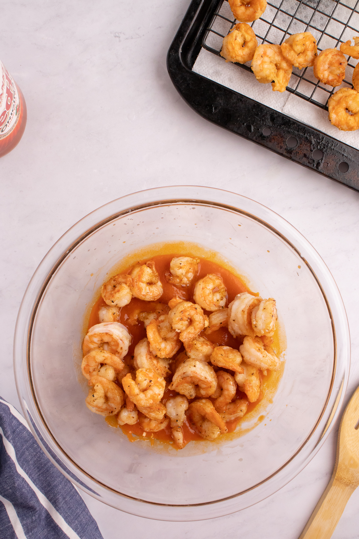 Crevettes frites enrobées de sauce Buffalo dans un bol à mélanger en verre.