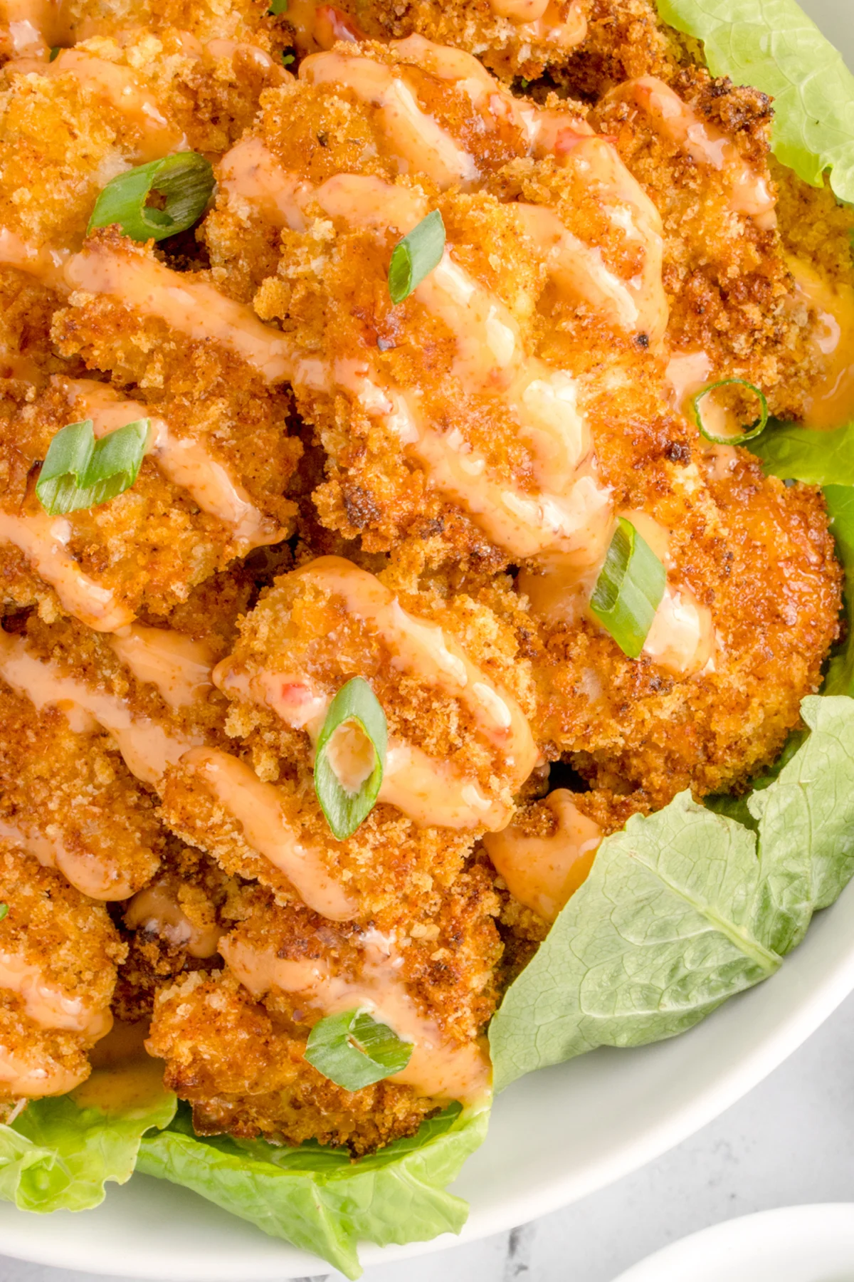 Un bol de service garni de feuilles de laitue verte croustillantes, puis rempli de crevettes croustillantes panées et frites à l'air arrosées de sauce bang bang.