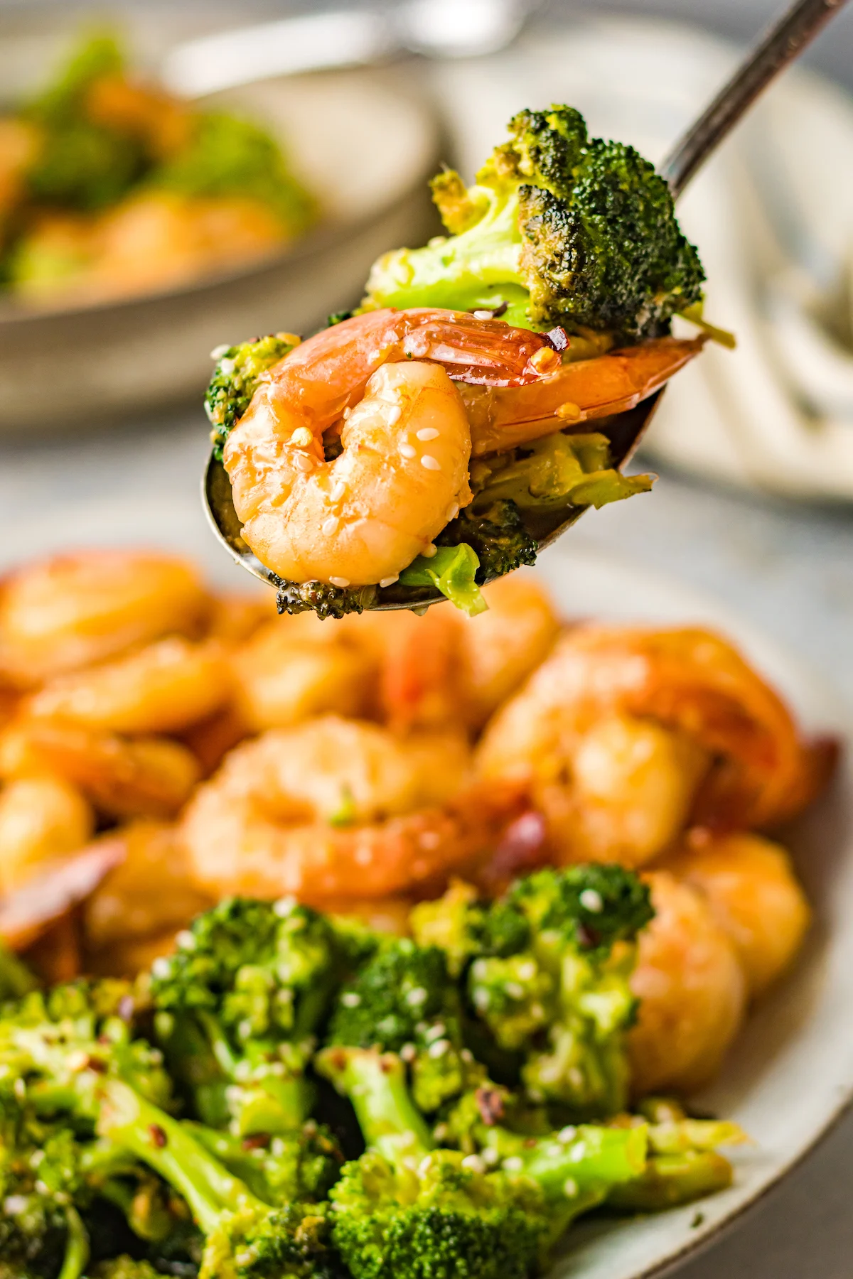 Une cuillère contient des crevettes et du brocoli cuits. L’assiette est floue en arrière-plan.