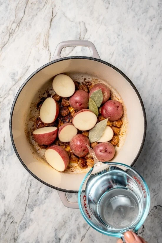 Verser de l'eau dans un four hollandais avec des feuilles de laurier et des pommes de terre