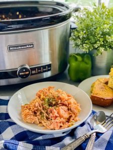White circular bowl filled with rice, shrimp, sausage, and chicken with a slow cooker in the background.