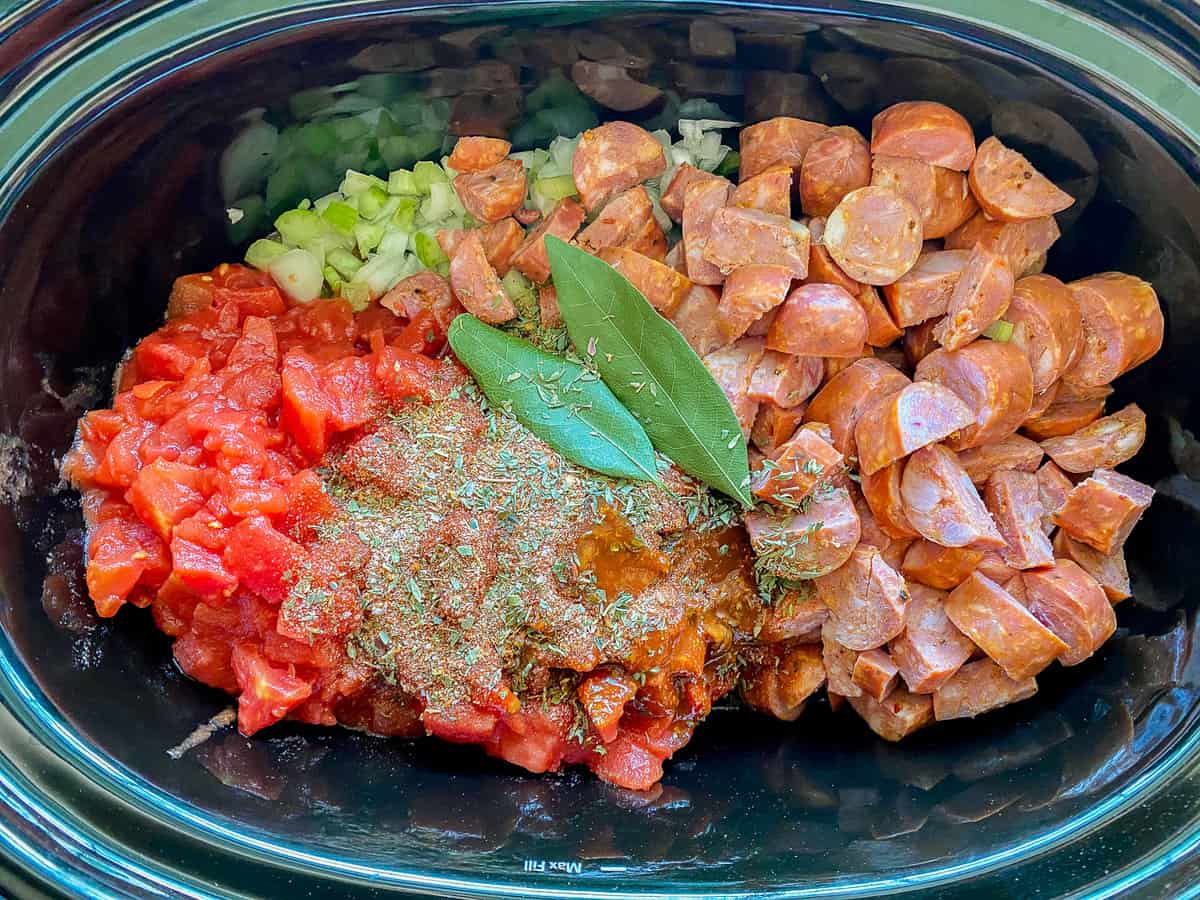 Mijoteuse ovale noire avec saucisses en dés, oignons, tomates et épices.