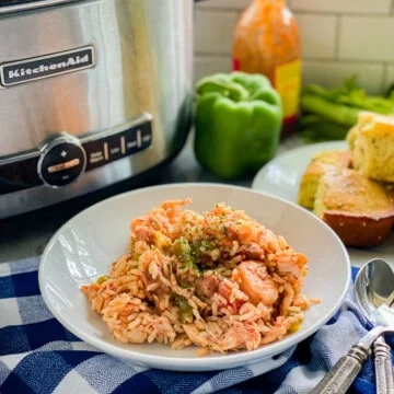 Bol blanc rempli de riz, de crevettes et de saucisses avec une cuillère à côté.
