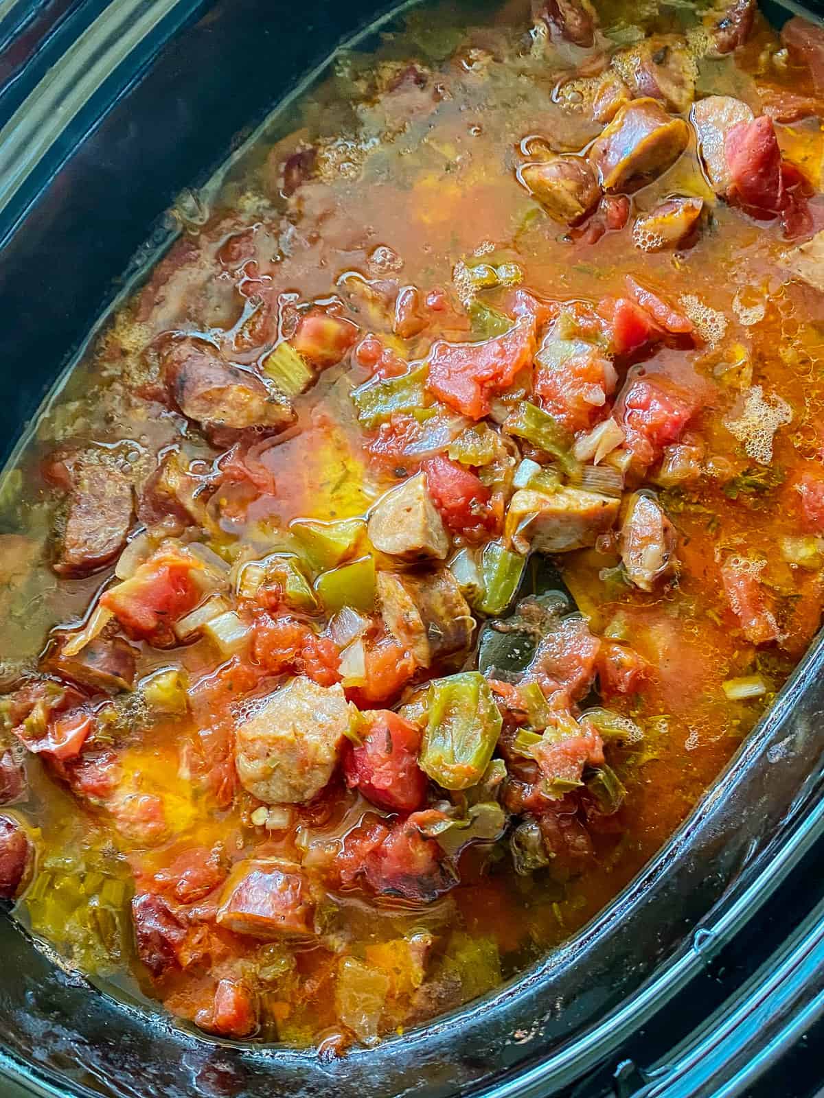Mijoteuse ovale noire avec saucisses et légumes.
