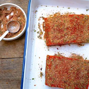 salmon rub in a bowl near a sheet pan of salmon that have dry rub on them