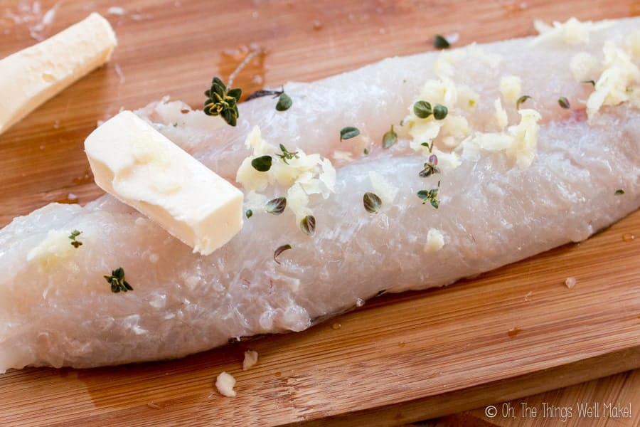Un filet de merlu avec du beurre, du thym et de l'ail dessus.