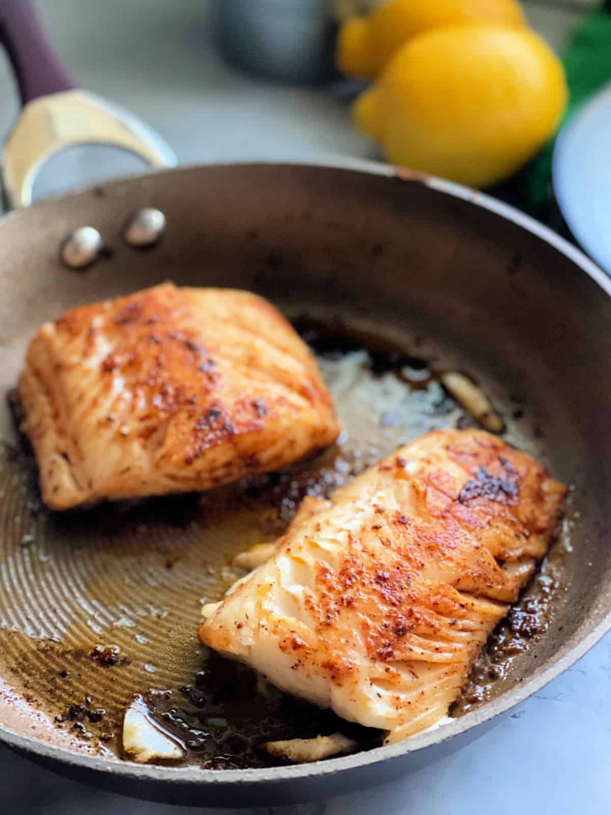 Deux filets de morue noire cuisant dans une poêle