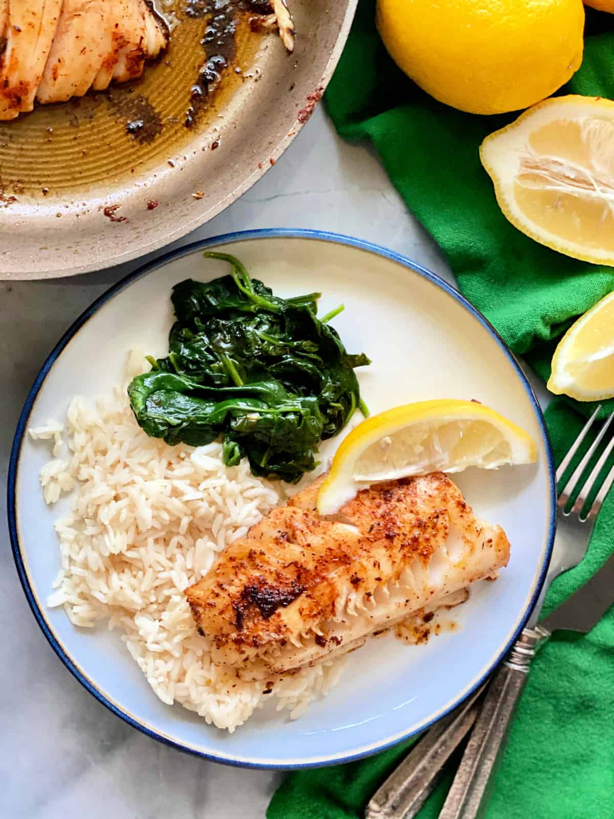 Vue de dessus de morue noircie, de riz blanc, d'épinards et d'une tranche de citron sur une assiette blanche