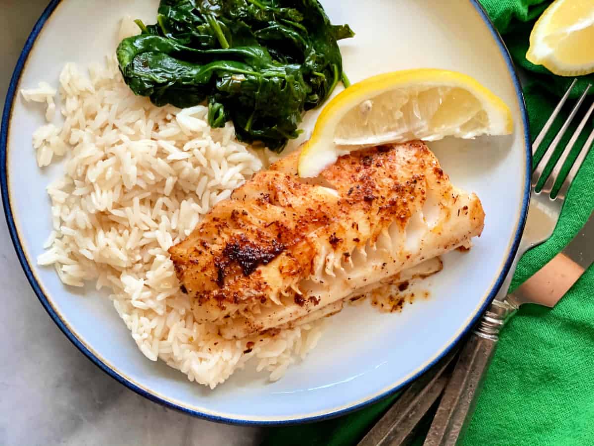 Vue de dessus de morue noircie, de riz blanc, d'épinards et d'une tranche de citron sur une assiette blanche