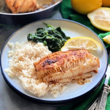 Assiette blanche avec un morceau de morue, du riz blanc, des épinards et un citron.