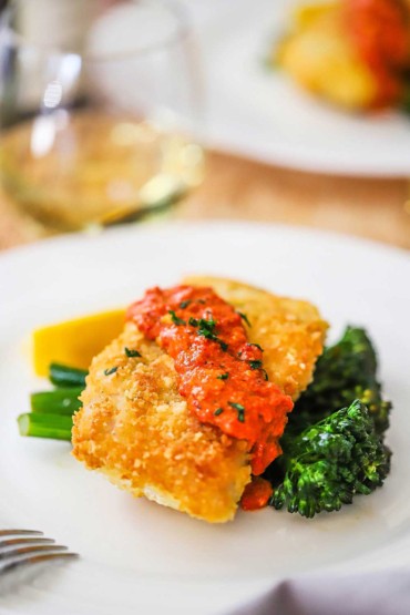 Une assiette blanche remplie de morue en croûte de parmesan et de romesco reposant sur des broccolini sautés.