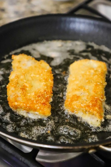 Deux filets de cabillaud en croûte de parmesan légèrement frits dans une poêle antiadhésive avec de l'huile bouillonnante.