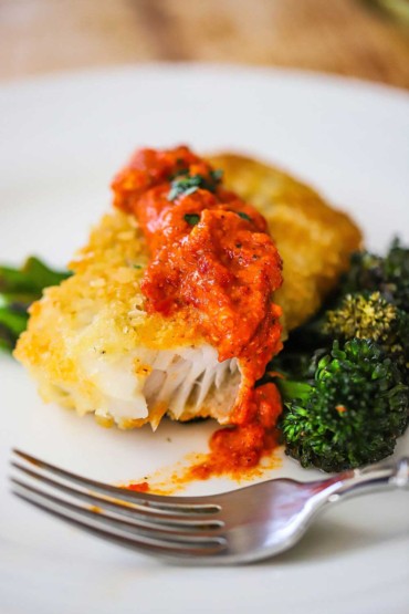 Une vue rapprochée de la morue en croûte de parmesan garnie de sauce romesco et une bouchée de celle-ci a disparu.