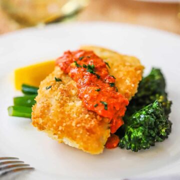 Une assiette blanche remplie de morue en croûte de parmesan et de romesco reposant sur des broccolini sautés.