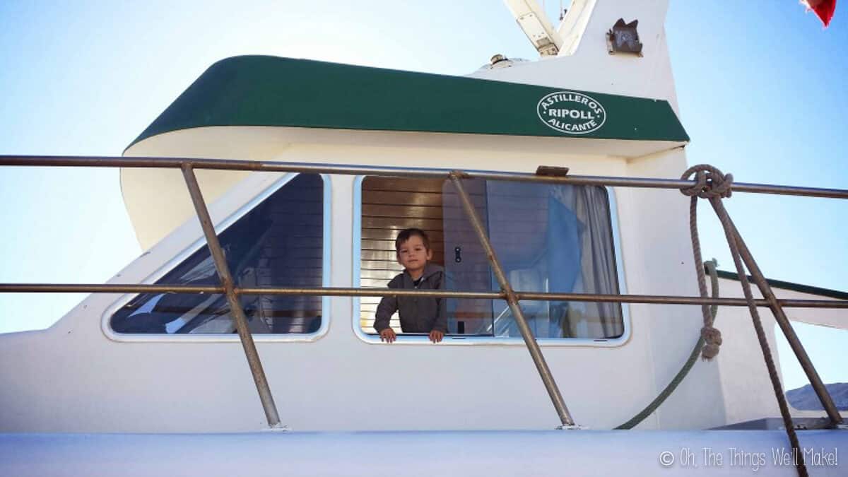 Un jeune garçon regarde par la fenêtre d’un bateau de pêche blanc.