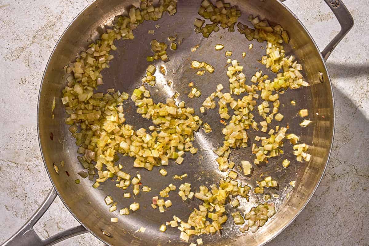 Les échalotes hachées pour les pâtes au homard étant sautées dans une poêle.
