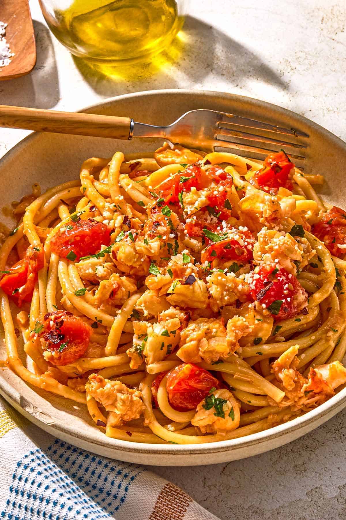 Pâtes au homard dans un bol avec une fourchette à côté d'une bouteille d'huile d'olive.