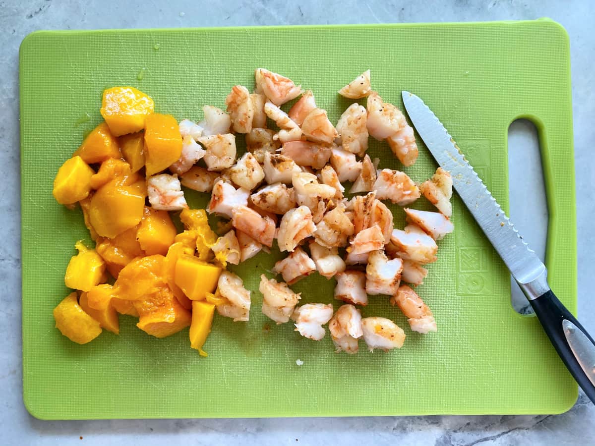 Planche à découper verte avec crevettes hachées et mangues avec couteau dentelé.