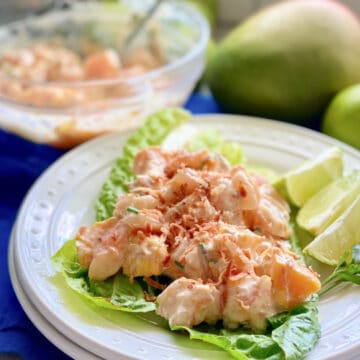 Assiette blanche avec laitue et salade de crevettes à la mangue sur le dessus.