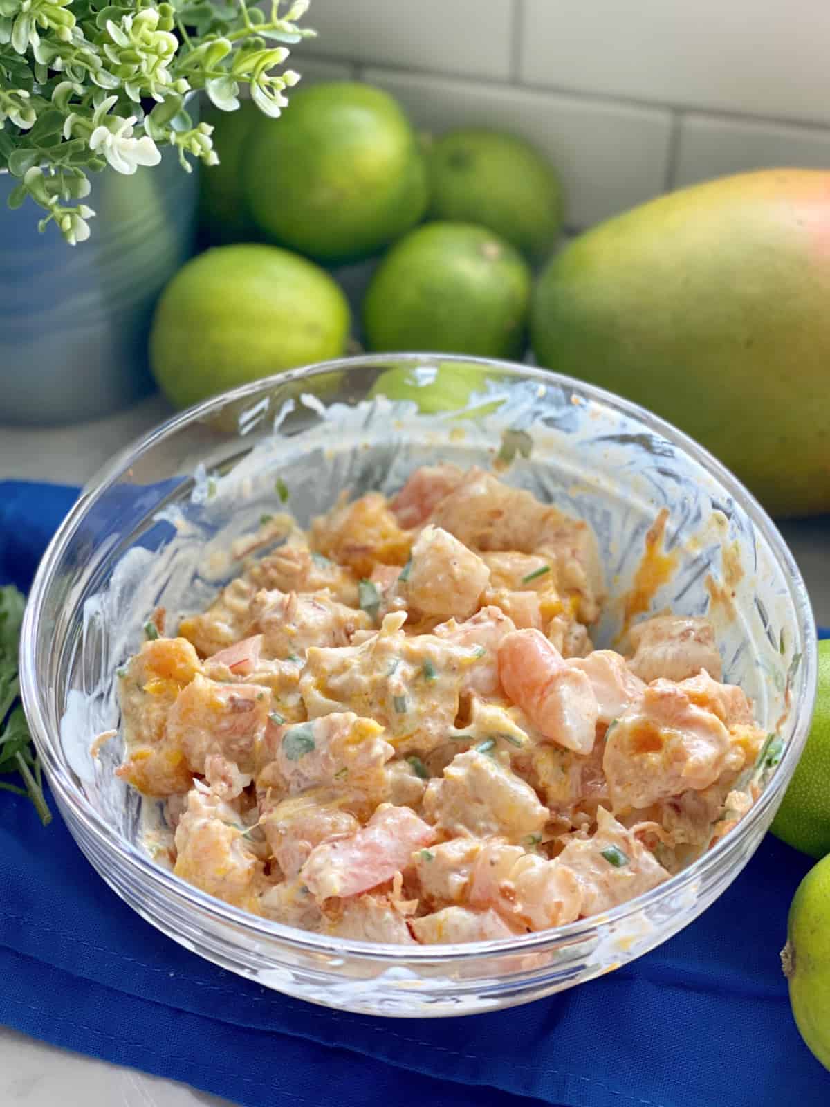 Bol en verre sur un tissu bleu rempli de salade de crevettes à la mangue.