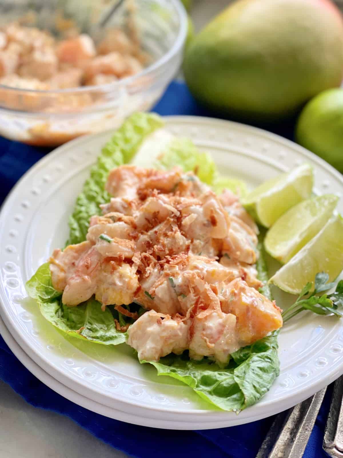 Gros plan de feuilles de laitue avec salade de crevettes et quartiers de citron vert.
