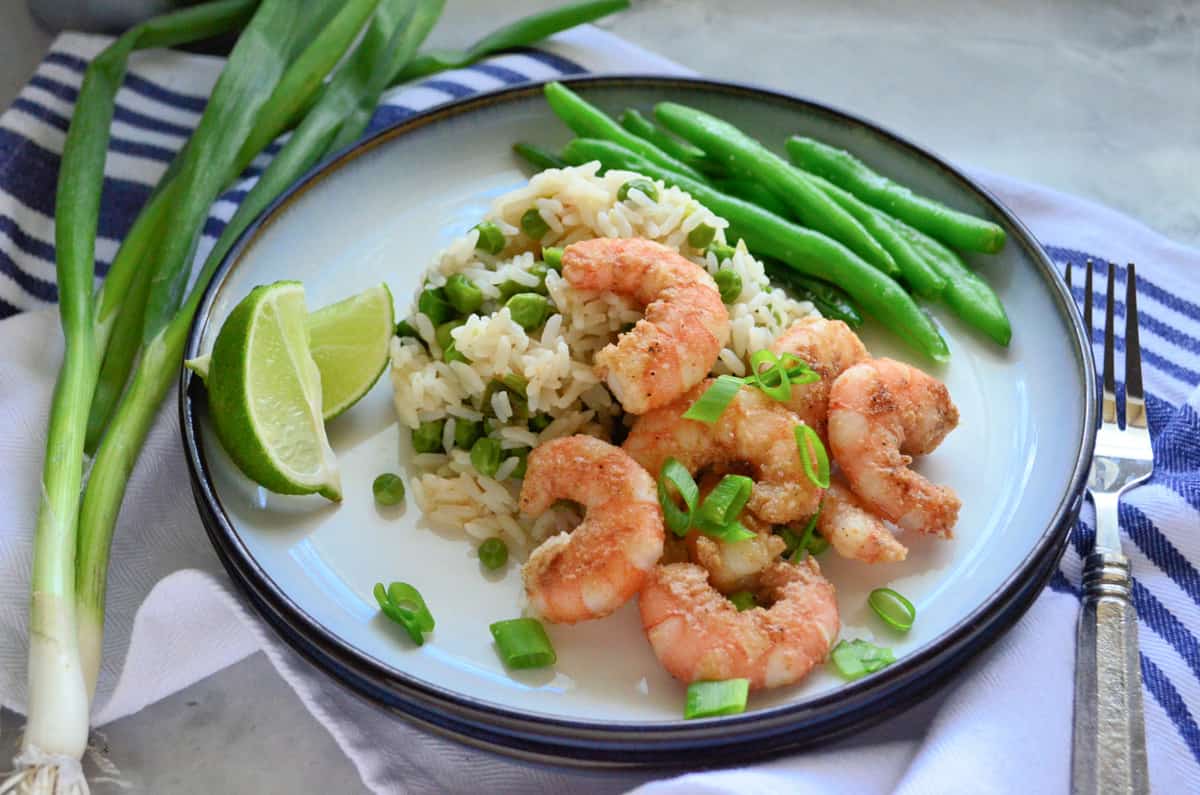 Assiette ronde blanche avec crevettes, riz, oignons verts et haricots verts sur une assiette posée sur un torchon.